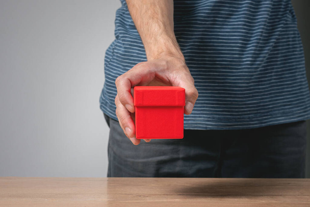 Red gift box in male hand on gray background. - Zdjęcie, obraz