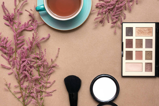 Make up concept flat lay background. Make up brushes and cosmetics, cup of tea and a blooming tamarix flowers on a brown paper background. - Foto, Imagen