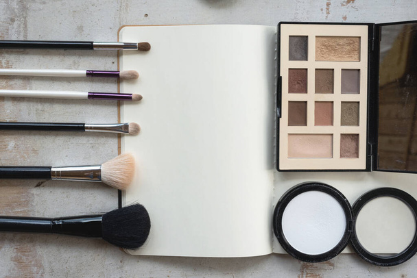 Open blank page notebook template, make up brushes and a eye shadows palette on a white wooden table flat lay background. - Foto, imagen