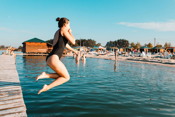 женщина прыгает с деревянного пирса в озерной воде. летний отдых
 - Фото, изображение