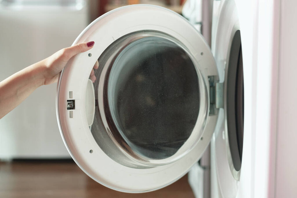 Woman opens the door of the washing machine. - Фото, зображення
