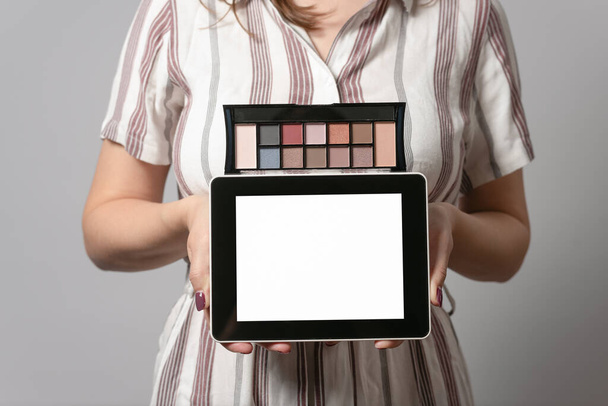 Makeup tips mockup. Beauty shop template. Woman holding in hands tablet computer with blank screen and a eye shadows palette isolated on gray background. - Foto, immagini