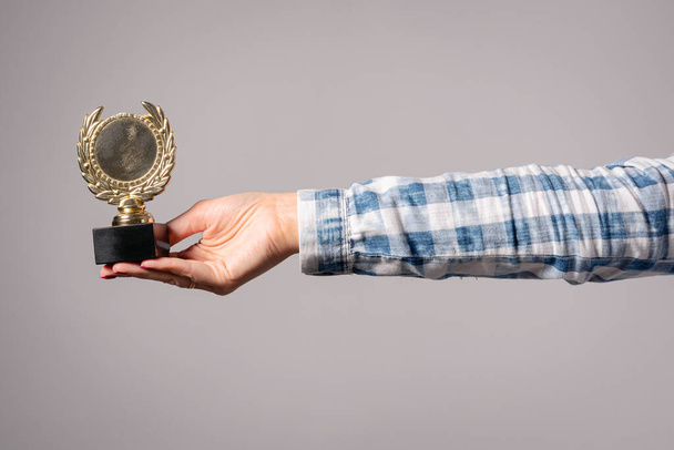 Golden medal award trophy in female hand isolated on gray background. - Foto, afbeelding