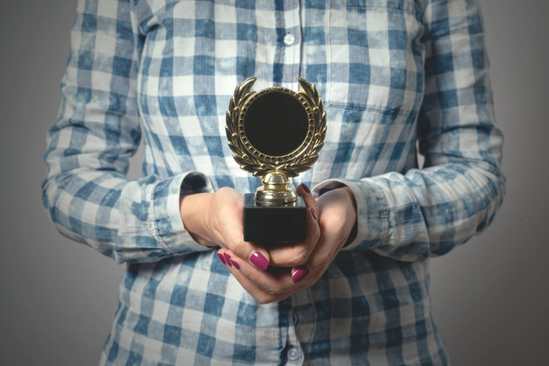 Golden medal in a female hands on gray background. Award ceremony concept. - Foto, afbeelding