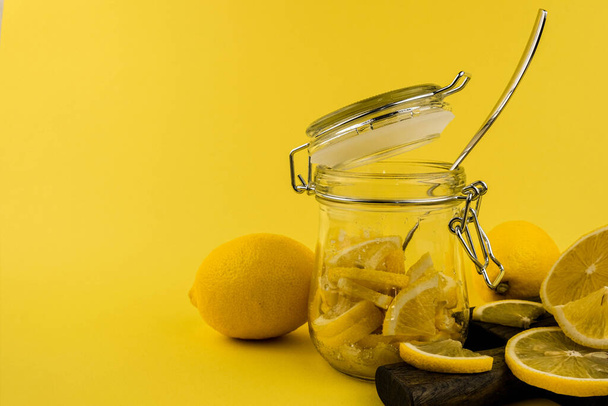Fresh lemons lie on a chopping wooden board on a yellow background with a glass jar - Valokuva, kuva