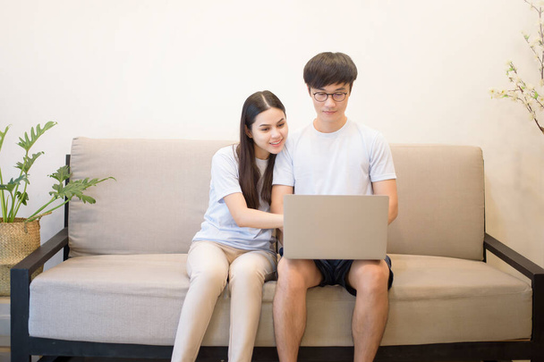 a young happy couple is relaxing and using a laptop on a sofa at home - Fotografie, Obrázek