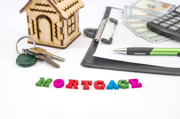 word Mortgage and wooden house, calculator, money and keys. A loan form with a pledge. Buying real estate or housing on credit. Mortgage credit lending. - Photo, Image