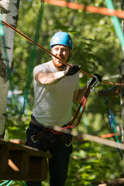 Aventura de cuerda - hombre caminando sobre el puente de cuerda unido al árbol con un gancho de seguro
 - Foto, Imagen