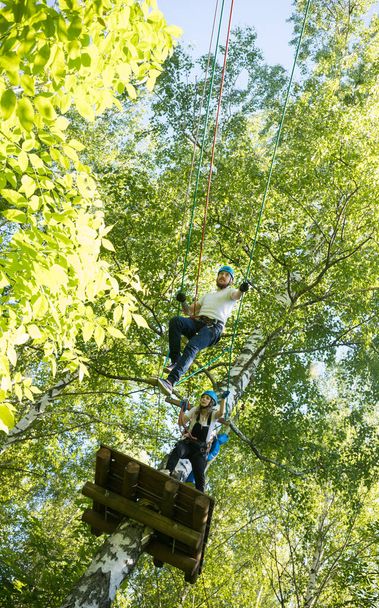 Aventura de cuerda - mujer y hombre teniendo un entretenimiento de cuerda en el bosque verde - de pie en lo alto y caminando sobre la cuerda
 - Foto, Imagen