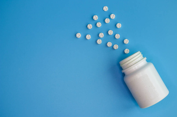 White round-shaped tablets are scattered from the bottle on a blue background. Medical concept, treatment of diseases and viruses, healthcare, pharmacy. Copy the space for the text. - Fotó, kép