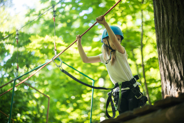 Aventura de cuerda: una niña camina sobre el puente de cuerda desde el soporte y sostiene las cuerdas con las manos
 - Foto, Imagen