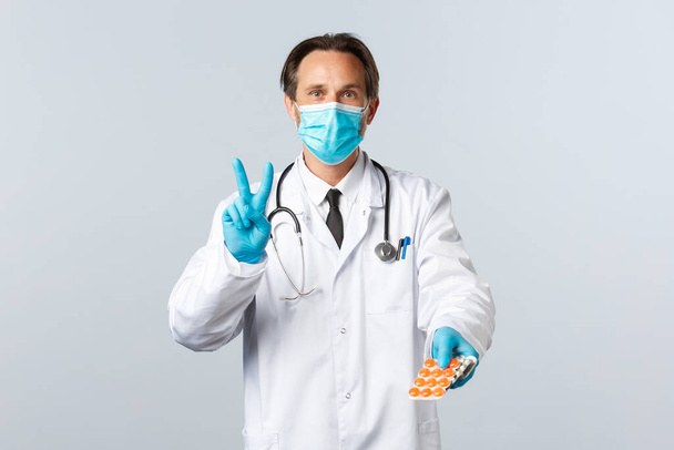 Covid-19, preventing virus, healthcare workers and vaccination concept. Doctor in medical mask and gloves prescribe take pills two times a day, show twice and medication, white background - Photo, Image
