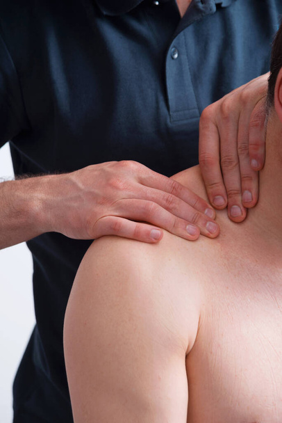 Αρσενικός φυσικοθεραπευτής πιέζει έναν άνθρωπο στον ώμο κάνοντας βαθύ μασάζ στο λαιμό του. - Φωτογραφία, εικόνα