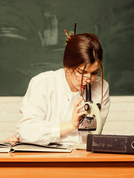 Laboratory testing. Smart student look in microscope in school laboratory. Pretty woman doing laboratory research in chemistry or biology. Supplied with new up-to-date laboratory equipment - Foto, Bild