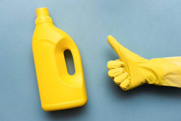 Detergent bottle and hand in the glove is showing a thumbs up gesture on the blue background. - Photo, image