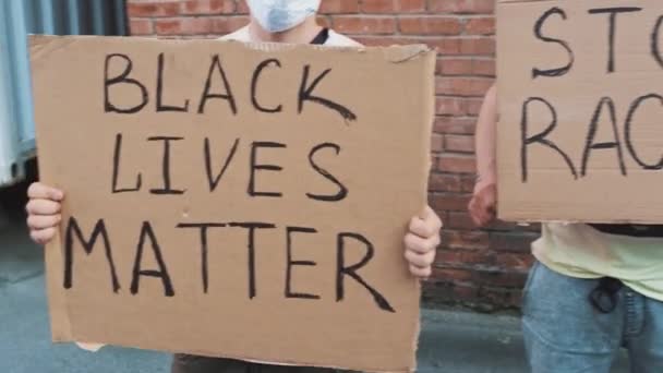 Quatre hommes caucasiens se tiennent contre un mur rouge avec des affiches en carton dans leurs mains avec des inscriptions : Black lives matter, Stop racisme, All lives matter, White lives matter - Séquence, vidéo