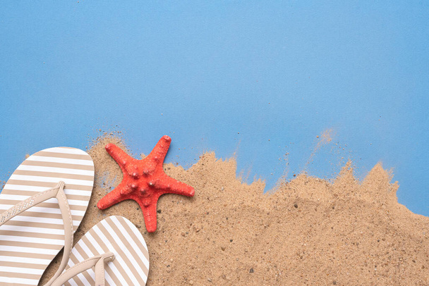 Sand beach, red starfish and flip flops on blue background with copy space. Summer vacation concept. Top view. - Valokuva, kuva
