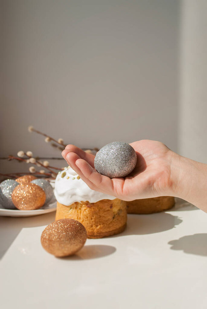Ruka drží stříbrné vejce na velikonočních koláčích a třpytivé vejce pozadí - Fotografie, Obrázek