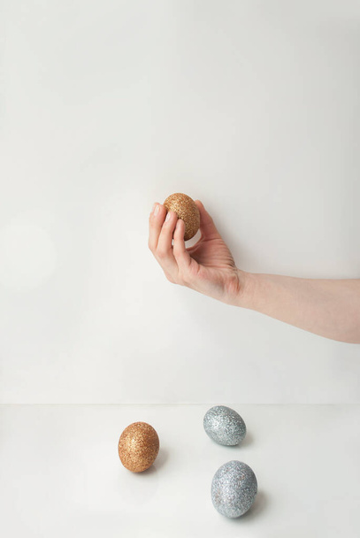 Minimalistic shot of women's hands holding golden egg in front of a wall - Fotoğraf, Görsel