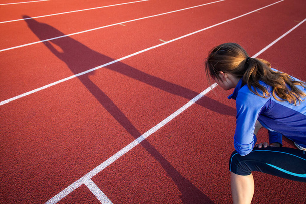 Pretty female runner stretching before her run at a track and field stadium - 写真・画像