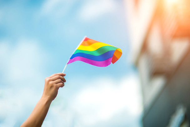 Feminine hand wearing a gay pride bracelet with rainbow flags against the sky. LGBT people, same-sex relationships and homosexual concepts  - Photo, Image