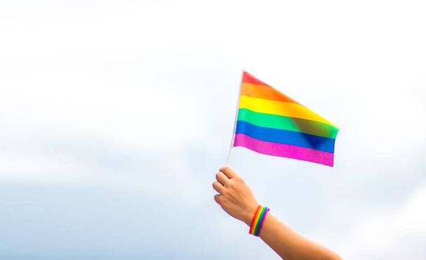  v ruce s náramkem gayské hrdosti s duhovými vlajkami proti obloze. LGBT osoby, vztahy stejného pohlaví a homosexuální pojmy  - Fotografie, Obrázek