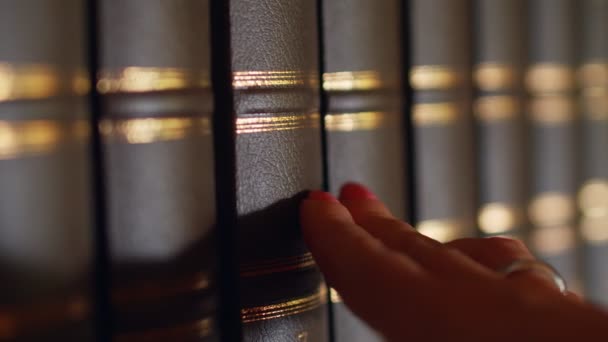 A női kéz kiválaszt egy könyvet a könyvtárban, fényűző bőrkötéssel. 4k - Felvétel, videó
