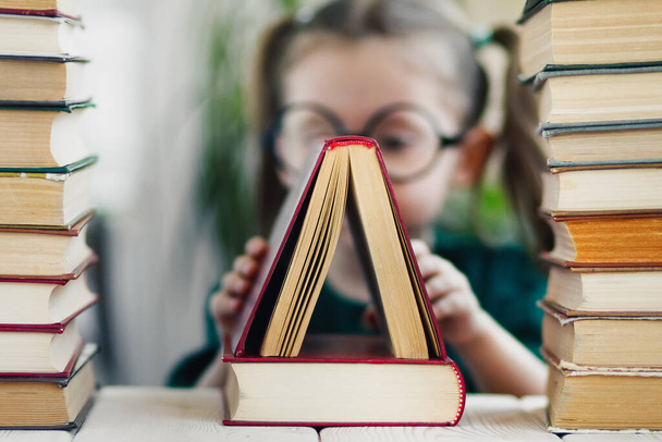 Close-up view on triangle shape to one book standing on another. Little girl on blurred background. - Φωτογραφία, εικόνα
