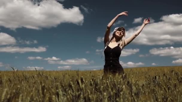 Buğday tarlasında dans eden kulaklıklı sarışın kadın. - Video, Çekim