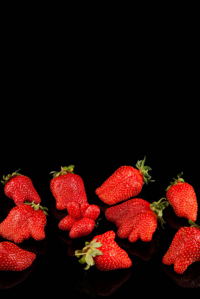 Ugly strawberries of an unusual shape on a dark background with reflection. Selective focus, vertical orientation, copy space. - Foto, imagen