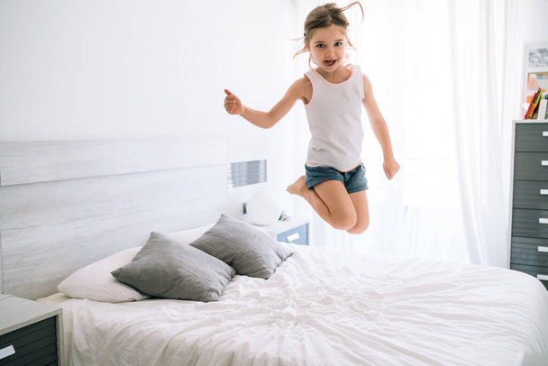 Kız covid 19 sırasında eğlencesine yatakta zıplıyor. Parmağıyla iyi gidiyor. - Fotoğraf, Görsel