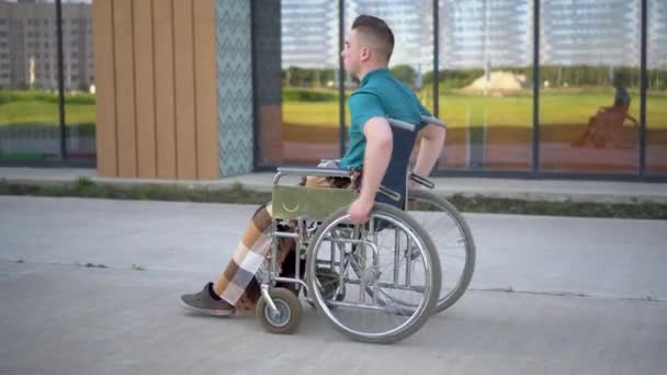 Junger Mann im Rollstuhl. Ein Mann fährt im Rollstuhl vor dem Hintergrund eines gläsernen Gebäudes. Spezielle Transportmittel für Behinderte. - Filmmaterial, Video