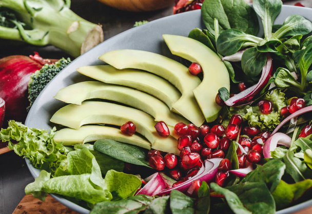 Healthy fresh salad with avocado, greens, arugula, spinach, pomegranate in plate over grey background. Healthy vegan food, clean eating, dieting, top view - Photo, Image