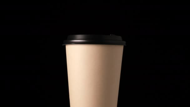 brown cardboard glass with a plastic lid rotates around its axis on a black background, disposable tableware - Footage, Video