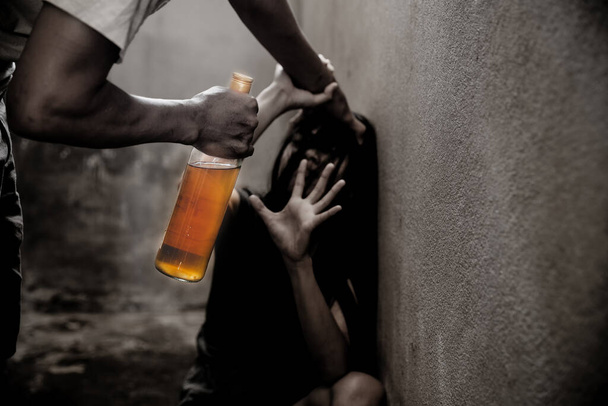 Γυναίκα θύμα ενδοοικογενειακής βίας και κακοποίησης. Γυναίκα φοβάται έναν άντρα που κρατάει μπουκάλι αλκοόλ. - Φωτογραφία, εικόνα