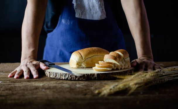 Manos masculinas cortando pan de trigo en la tabla de madera. Pan tradicional cortado en rodajas
 - Foto, imagen