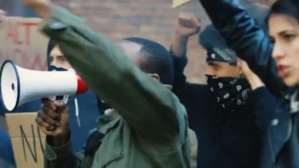 Mužští a ženské míšenci křičí slogany a protestují v USA proti rasismu a policejním aktům. Africký Američan vede a křičí v megafonu a běloška drží plakát. - Záběry, video