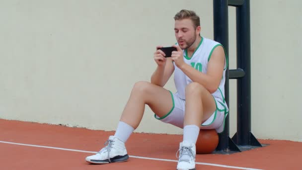 Basketball Fan Reaction Concept - Aufgeregter Basketballspieler im Basketball-Outfit beobachtet sein Lieblingsteam auf dem Smartphone, 4k Zeitlupe - Filmmaterial, Video