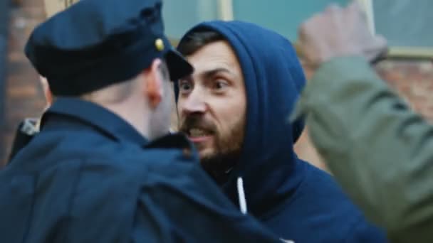 Giovane manifestante caucasico in cappuccio urlando, urlando e attaccando poliziotto a manifestazione contro la violenza e il razzismo. Poliziotti che usano la forza per calmare i ribelli maschi. - Filmati, video