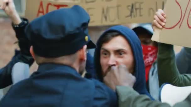 Kavkazský mladý muž v kapuci křičí, křičí a útočí na policistu při projevu násilí a rasismu. Policisté používají sílu, aby zklidnili mužské rebely. Policie bojuje na povstání. - Záběry, video