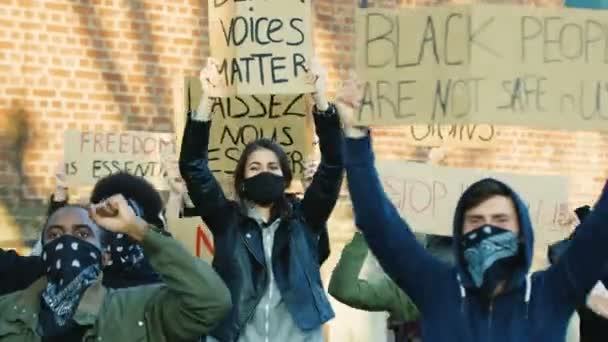 人種差別や警察の暴力に抗議する仮面の顔をした多民族の若い男性と女性の抗議者。デモでは、ポスターを叫んでモットーを持つ混合レースの人々。平等な人権の概念 - 映像、動画