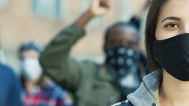 Nahaufnahme des halben Gesichts einer jungen kaukasischen schönen Frau in schwarzer Maske, die bei Straßenkrawallen direkt in die Kamera schaut. Porträt eines Mädchens. Demonstrantin bei Demonstration für Menschenrechte. - Filmmaterial, Video