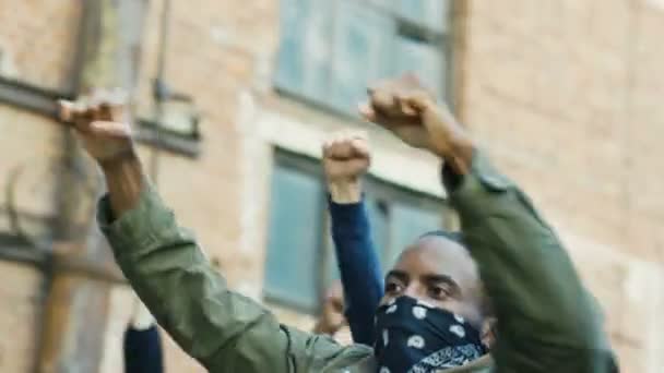 Manifestantes multiétnicos jóvenes hombres y mujeres con máscaras que protestan contra el racismo y la violencia policial. Rebeldes de razas mixtas con carteles gritando consignas a la manifestación en Estados Unidos. Activistas políticos
. - Metraje, vídeo