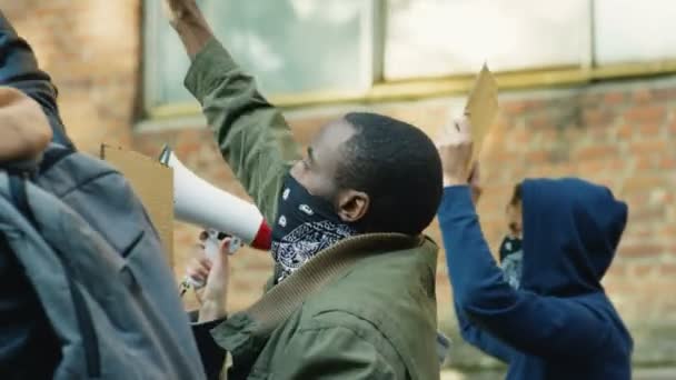 Visszapillantás afro-amerikai férfi tüntetőre, aki többnemzetiségű tömegben sikoltozik és kiabál a rendőrség és a kormány elleni utcai lázadás miatt. Vegyes fajú tüntetők és lázadók háta. - Felvétel, videó