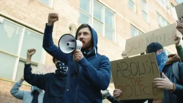 Kaukasische jonge man leider schreeuwen motto 's in megafoon op straat in menigte bij protest tegen racisme in de VS. Actieve gemengde-rassen demonstranten schreeuwen eisen. Man leidt tot rebellie. - Video