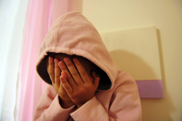 Молодая девушка в толстовке, жертва домашнего насилия, закрывающая лицо в спальне
. - Фото, изображение
