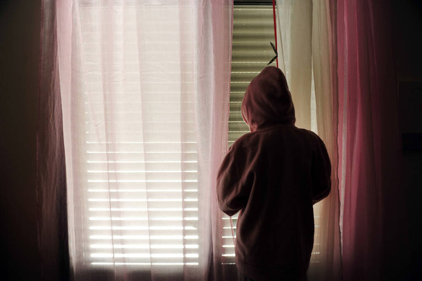 Молода дівчина, одягнена в светр жертви домашнього насильства, дивиться на вікно своєї спальні
. - Фото, зображення