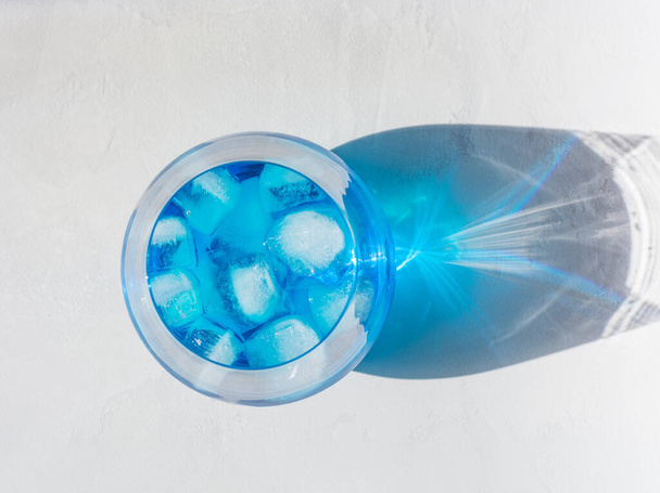 Succo di ghiaccio di pisello farfalla blu con cubetti di ghiaccio in un vetro trasparente si erge su un tavolo grigio in una giornata di sole. primo piano, vista dall'alto, bella ombra. - Foto, immagini