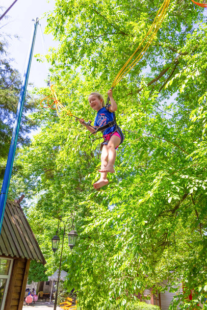 Usmívající se šťastná dívka skákání s bungee v trampolíně v parku proti zeleným stromům - Fotografie, Obrázek