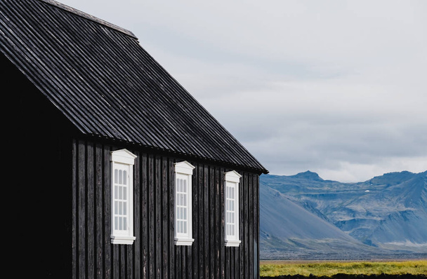 Czarny kościół na łące i polu na Islandii. Zbliżenie czarnych ścian i białych platform okiennych. - Zdjęcie, obraz